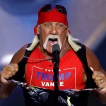 Imagem do lutador Hulk Hogan com sua bandana vermelha característica, óculos escuros e expressão séria, em fundo escuro e dramático.