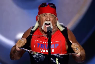 Imagem do lutador Hulk Hogan com sua bandana vermelha característica, óculos escuros e expressão séria, em fundo escuro e dramático.