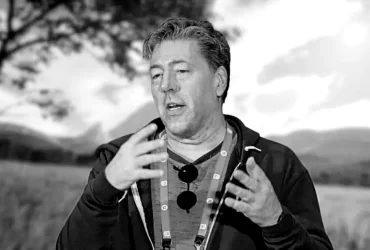 Imagem em preto e branco de Julian LeFay, desenvolvedor de jogos, gesticulando enquanto fala, com cenário natural desfocado ao fundo