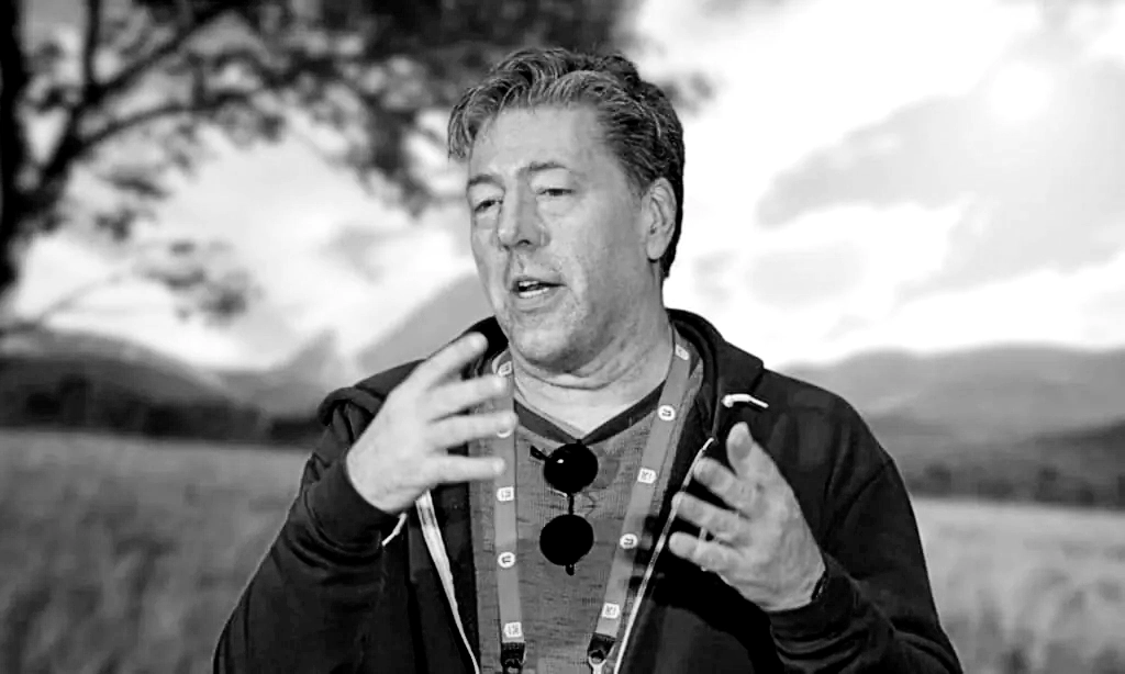 Imagem em preto e branco de Julian LeFay, desenvolvedor de jogos, gesticulando enquanto fala, com cenário natural desfocado ao fundo