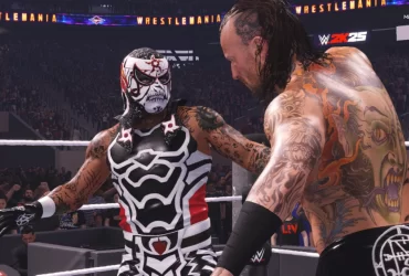 Dois lutadores se encaram no ringue durante uma luta em WWE 2K25, com o logo de WrestleMania e o público ao fundo. Um deles veste uma máscara com pintura de caveira, enquanto o outro exibe tatuagens detalhadas nas costas.