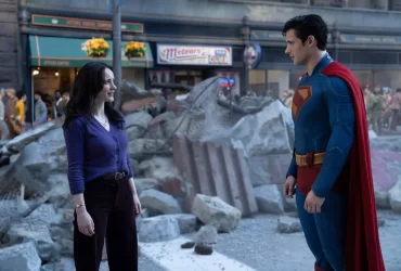 Imagem de Superman (David Corenswet) em uma pose heroica, com Lois Lane (Rachel Brosnahan) ao fundo, capturando a química entre os dois personagens no filme Superman, dirigido por James Gunn