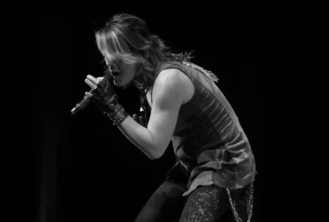 Cantor japonês se apresenta no palco segurando um microfone com as duas mãos, em foto em preto e branco.