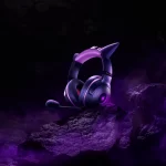 Headset Razer Kraken Kitty V2 – Gengar Edition iluminado em tons de roxo, exibido sobre rochas escuras com fumaça púrpura, remetendo à estética fantasmagórica do Pokémon Gengar.