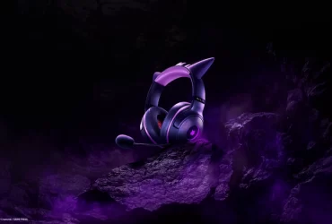 Headset Razer Kraken Kitty V2 – Gengar Edition iluminado em tons de roxo, exibido sobre rochas escuras com fumaça púrpura, remetendo à estética fantasmagórica do Pokémon Gengar.