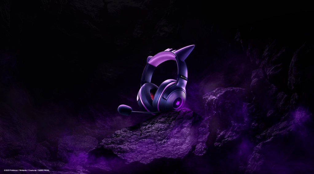 Headset Razer Kraken Kitty V2 – Gengar Edition iluminado em tons de roxo, exibido sobre rochas escuras com fumaça púrpura, remetendo à estética fantasmagórica do Pokémon Gengar.
