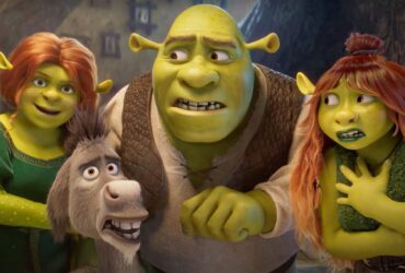 Cena animada de Shrek mostrando Shrek, Fiona, Burro e uma jovem ogra ruiva, todos com expressões de surpresa e apreensão, dentro de uma casa iluminada.