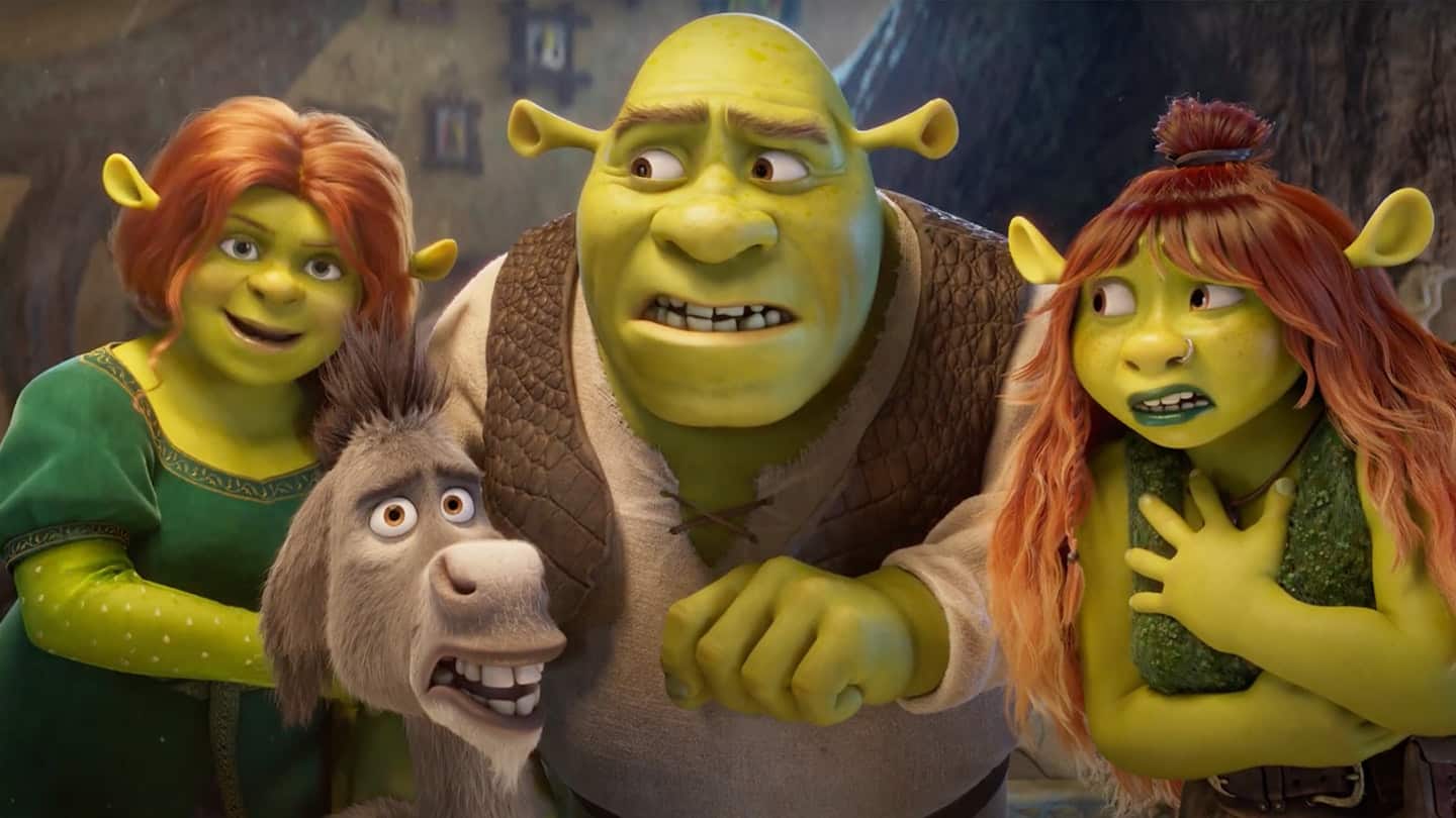 Cena animada de Shrek mostrando Shrek, Fiona, Burro e uma jovem ogra ruiva, todos com expressões de surpresa e apreensão, dentro de uma casa iluminada.