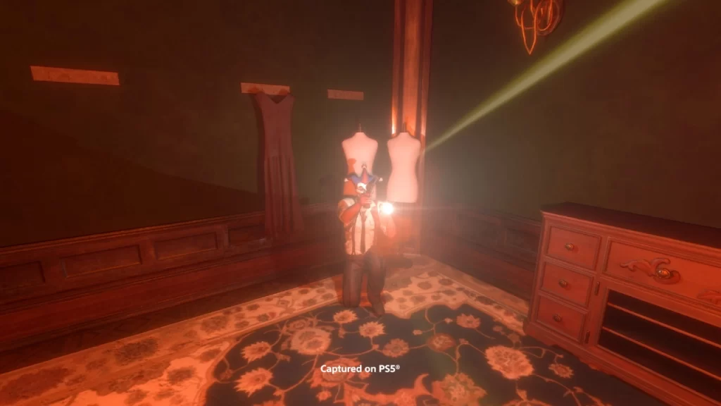 Cena de gameplay de Midnight Murder Club no PS5 mostrando um personagem ajoelhado em um quarto escuro, segurando uma lanterna e um revólver, iluminando manequins e parte da mobília.