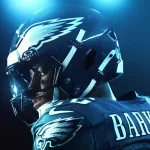 Close-up de um atleta da NFL com uniforme dos Philadelphia Eagles, visto de perfil com capacete preto e logo da águia, pintura no rosto e iluminação azul intensa ao fundo.