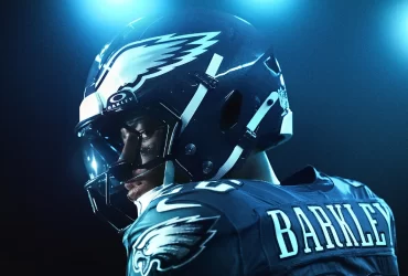 Close-up de um atleta da NFL com uniforme dos Philadelphia Eagles, visto de perfil com capacete preto e logo da águia, pintura no rosto e iluminação azul intensa ao fundo.