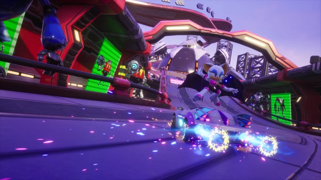 Rouge the Bat aparece em ação em Sonic Racing: CrossWorlds, pulando do carro esportivo roxo com rodas brilhantes em chamas azuis durante uma curva em pista futurista cheia de robôs e estruturas metálicas.