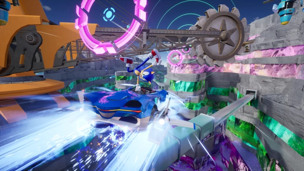 Sonic pilota um carro azul em alta velocidade em Sonic Racing: CrossWorlds, realizando uma manobra enquanto passa por engrenagens gigantes e portais circulares brilhantes em um cenário montanhoso com cristais coloridos.