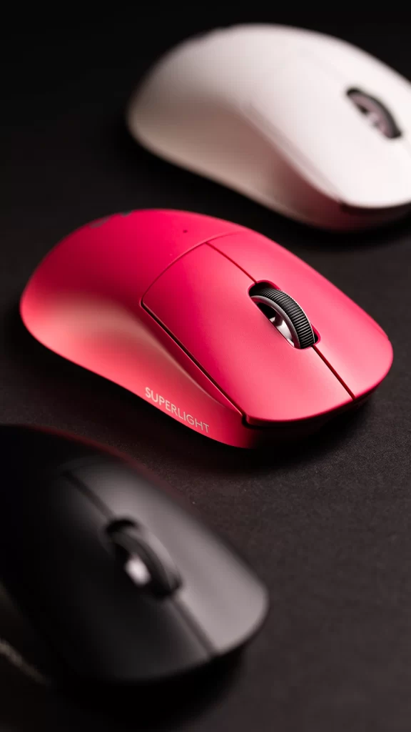 Três mouses Logitech G PRO X SUPERLIGHT 2c LIGHTSPEED nas cores rosa, branco e preto, posicionados sobre superfície escura, com foco no modelo rosa em primeiro plano.