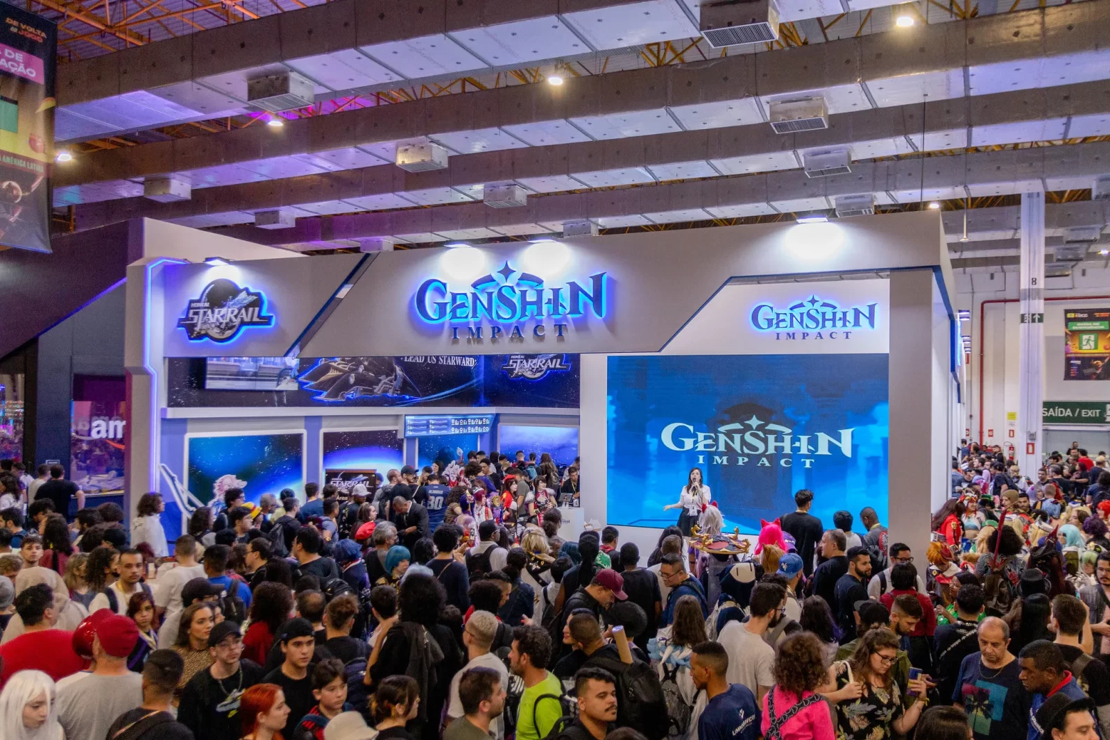 Estande de Genshin Impact lotado de visitantes na Brasil Game Show 2023, com telão exibindo o logo do jogo e fãs reunidos para participar das ativações.
