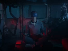 Personagem de Stranger Things 5 senta no chão com os olhos vendados em um ambiente escuro tomado por raízes e luzes vermelhas do Mundo Invertido.