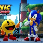 PAC-MAN e Sonic the Hedgehog lado a lado em um cenário colorido de Sonic Racing: CrossWorlds, com paisagem verde ao fundo e o logo do jogo no canto da imagem.
