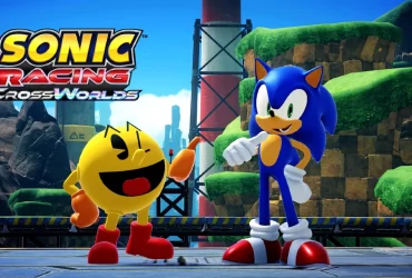 PAC-MAN e Sonic the Hedgehog lado a lado em um cenário colorido de Sonic Racing: CrossWorlds, com paisagem verde ao fundo e o logo do jogo no canto da imagem.
