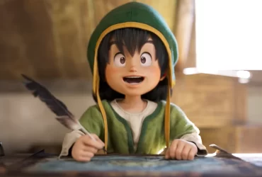 Personagem infantil de DRAGON QUEST VII Reimagined com chapéu verde e pena na mão, sorrindo enquanto escreve sobre uma mesa em ambiente iluminado.