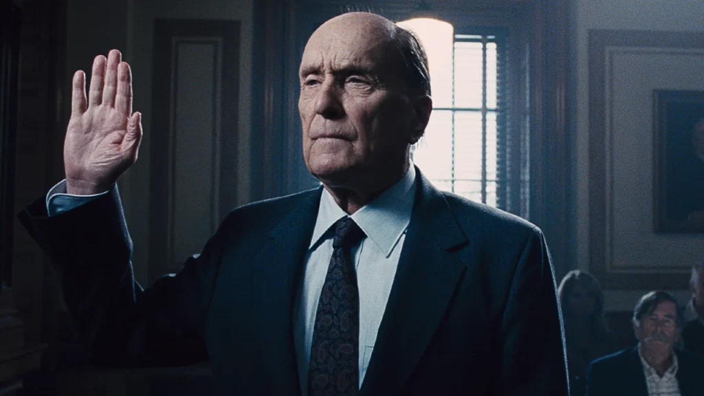 Robert Duvall, usando terno escuro, levanta a mão direita durante juramento em um tribunal no filme O Juiz.