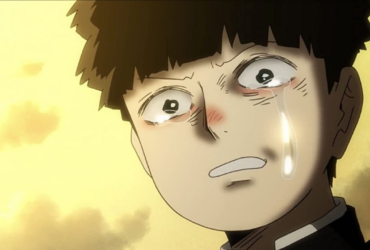 Close no rosto de Mob, personagem de Mob Psycho 100, com lágrimas escorrendo e expressão de dor e vulnerabilidade, em um fundo iluminado em tons amarelos.