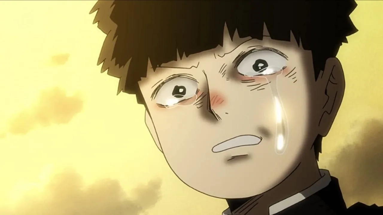 Close no rosto de Mob, personagem de Mob Psycho 100, com lágrimas escorrendo e expressão de dor e vulnerabilidade, em um fundo iluminado em tons amarelos.