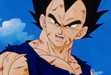 Vegeta em primeiro plano, com o uniforme rasgado e arranhões pelo corpo, expressão tensa e determinada, olhando de lado sob um céu azul com nuvens, sugerindo exaustão e inquietação mesmo depois da luta.