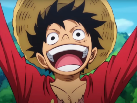 Monkey D. Luffy, personagem de One Piece, aparece sorrindo com a boca aberta e os braços erguidos, usando chapéu de palha e camisa vermelha, com céu azul e vegetação ao fundo.