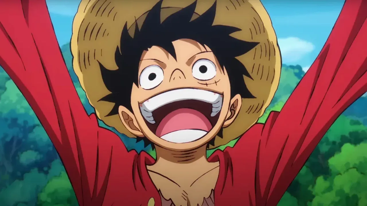 Monkey D. Luffy, personagem de One Piece, aparece sorrindo com a boca aberta e os braços erguidos, usando chapéu de palha e camisa vermelha, com céu azul e vegetação ao fundo.