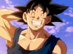 Goku, personagem de Dragon Ball, aparece sorrindo com os olhos fechados e os dentes à mostra, com a mão atrás da cabeça, usando roupa rasgada, com céu azul e nuvens ao fundo.