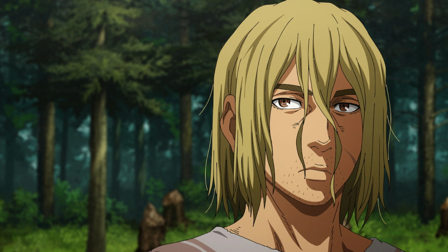 Thorfinn (Vinland Saga) em close, com cabelo loiro comprido e expressão cansada e reflexiva, em uma floresta ao fundo.