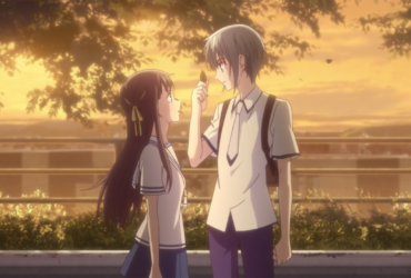 Cena de Fruits Basket ao entardecer: dois estudantes de uniforme, um rapaz de cabelo claro e uma garota de cabelo longo escuro, se encaram em uma rua arborizada com luz dourada; o rapaz segura uma folha entre os dedos, como um gesto delicado de aproximação.