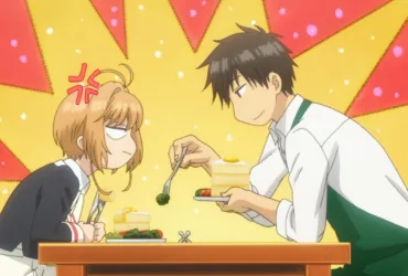 Cena de anime com Touya Kinomoto sentado à mesa, usando um avental verde, oferecendo um pedaço de brócolis com um garfo para Sakura Kinomoto, que está emburrada; o fundo é amarelo e vermelho, com clima cômico, sugerindo uma rotina doméstica onde o irmão mais velho cuida mesmo fingindo que não.