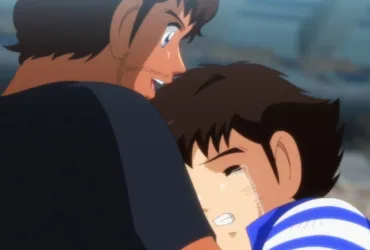 Cena de Captain Tsubasa (Super Campeões) em que Tsubasa, um garoto japonês emocionado e chorando, abraça Roberto, um homem brasileiro, em um estádio de futebol com arquibancadas desfocadas ao fundo. Imagem de Captain Tsubasa (Super Campeões) mostrando um japonês chorando nos braços de um brasileiro: Tsubasa abraça Roberto no estádio. A cena conversa com o clima de Brasil x Japão ao transformar rivalidade e contraste de estilos em algo mais humano — respeito, amizade e a vontade de “mais jogo” quando o apito final não basta.