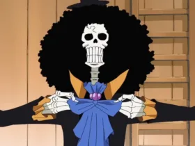 Brook, personagem esqueleto de One Piece, aparece de frente com um grande cabelo afro preto, casaco escuro com detalhes amarelos e laço azul no pescoço. Ele segura as lapelas da roupa em um ambiente de madeira, ao lado de uma cortina azul.