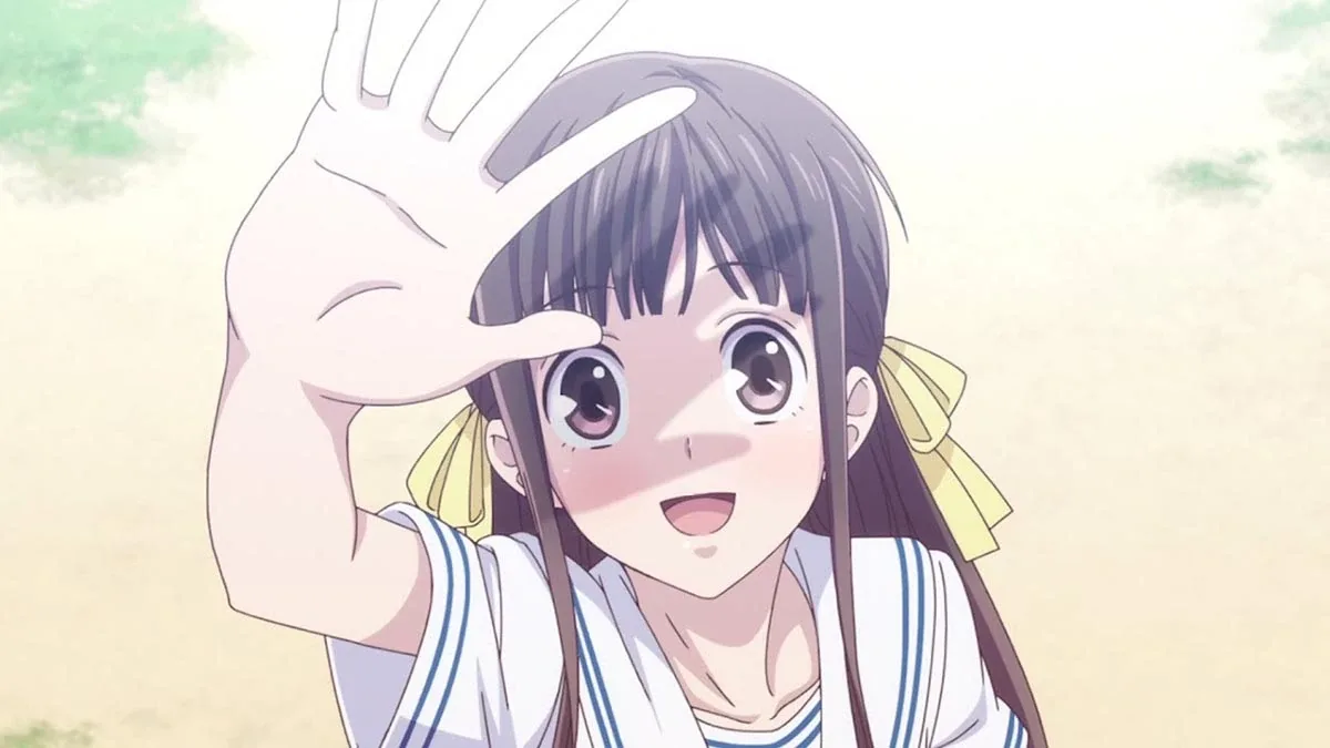 Tohru Honda, protagonista de Fruits Basket, aparece em primeiro plano sorrindo e levantando a mão diante do rosto, como se brincasse com a luz. Ela tem cabelos castanhos longos com laços amarelos e veste um uniforme escolar branco. O fundo claro e suave reforça a delicadeza, a alegria e a sensibilidade da personagem.