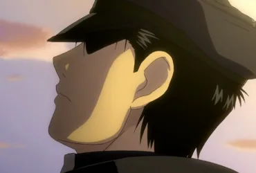 Roy Mustang, personagem de Fullmetal Alchemist: Brotherhood, aparece de perfil usando uniforme militar e boné escuro durante o enterro de Maes Hughes. A luz do fim de tarde ilumina parte de seu rosto enquanto seus olhos ficam escondidos pela sombra do boné, criando uma expressão contida de tristeza, culpa e despedida.