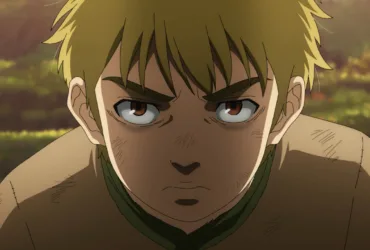 Thorfinn criança, personagem de Vinland Saga, aparece em close com expressão séria e determinada. Seus cabelos loiros estão desalinhados, há marcas de sujeira e pequenos ferimentos em seu rosto e roupas, e o cenário externo desfocado em tons quentes reforça o clima de jornada, conflito e alerta constante.