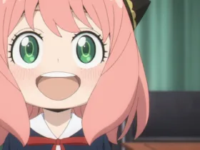 Anya Forger, personagem de Spy x Family, aparece em close sorrindo com os olhos verdes bem abertos. A garota tem cabelo rosa, presilhas pretas e douradas e usa uniforme escolar escuro com laço vermelho, diante de uma cortina verde.