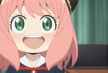 Anya Forger, personagem de Spy x Family, aparece em close sorrindo com os olhos verdes bem abertos. A garota tem cabelo rosa, presilhas pretas e douradas e usa uniforme escolar escuro com laço vermelho, diante de uma cortina verde.