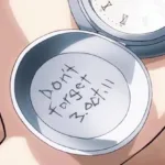 Mão segura o relógio de bolso prateado de Edward Elric aberto, com a inscrição “Don’t Forget 3.Oct.11” gravada na parte interna da tampa.
